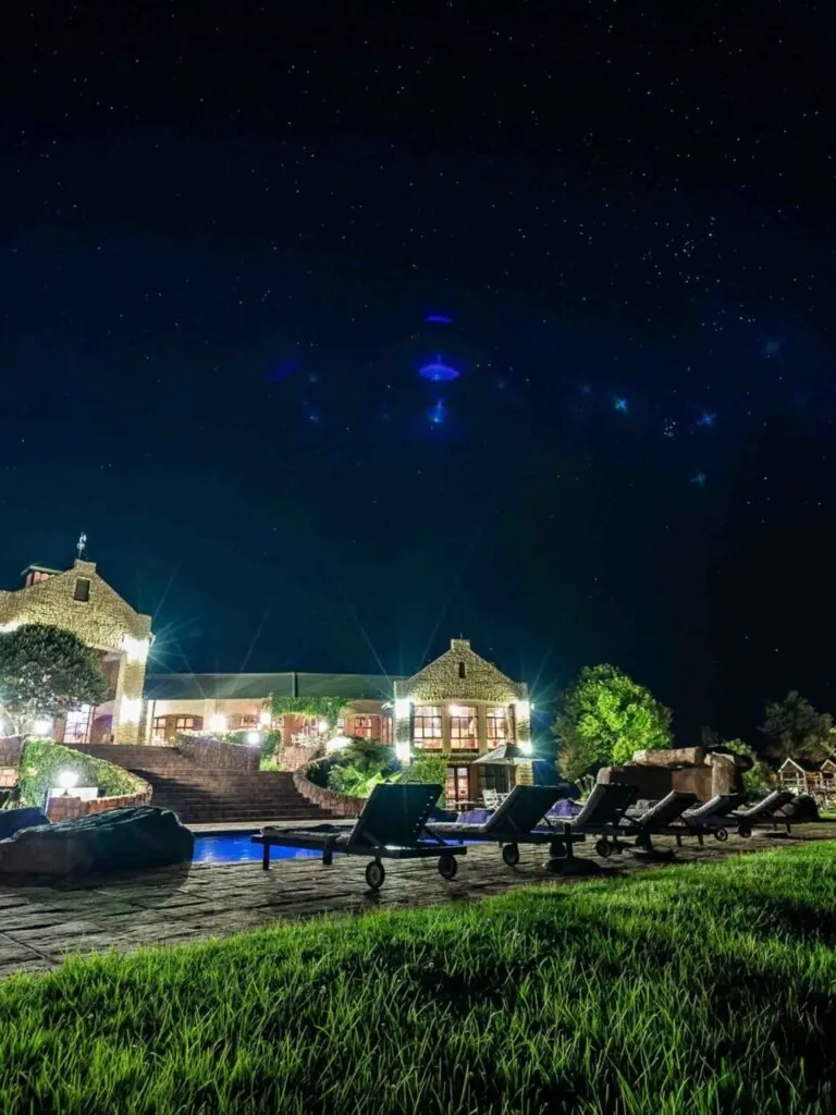 Night view of a lit house with lawn chairs and a starry sky