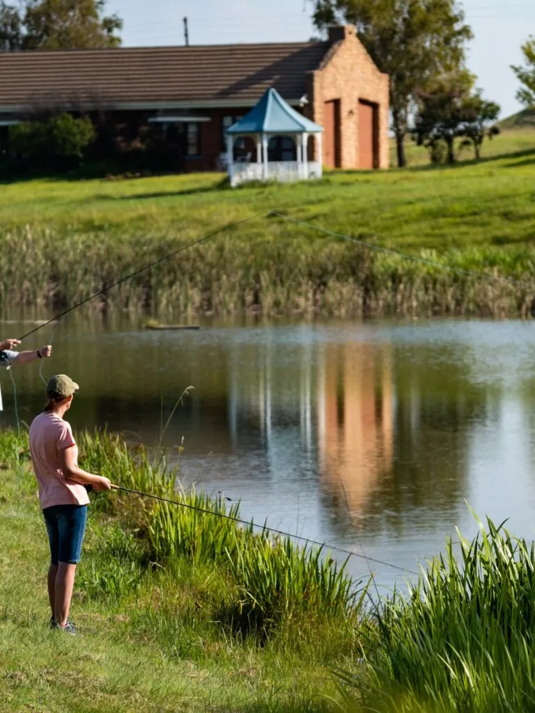 Person fishing by a pond with a house in the background