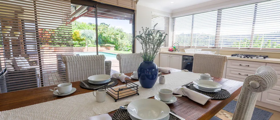 Dining table set with dishes and a vase overlooking a pool and garden