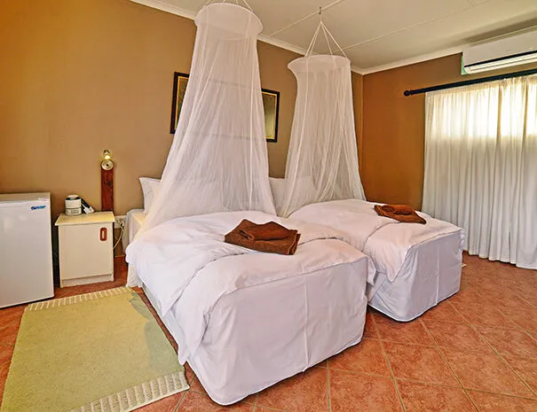Two beds with mosquito nets in a tiled room with a refrigerator