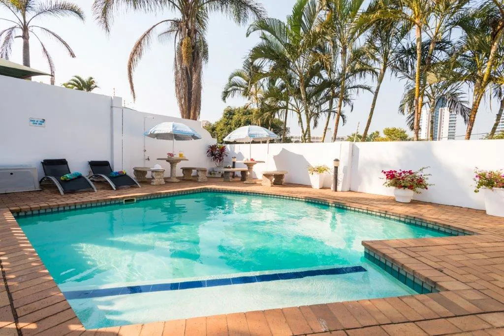 Swimming pool with lounge chairs umbrellas and palm trees in a sunny courtyard