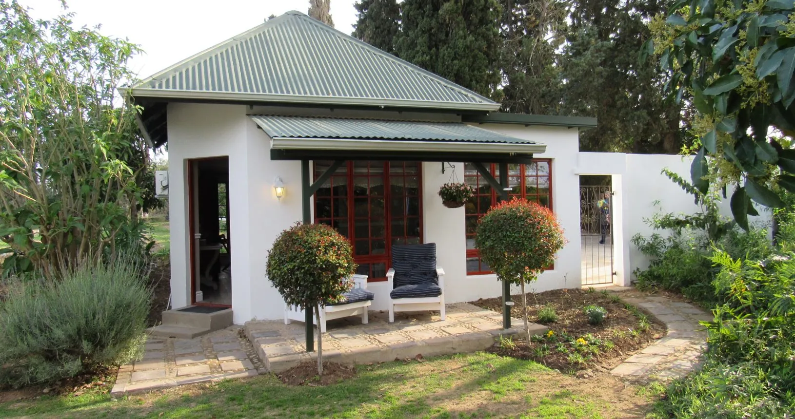 Small white house with green roof garden and pathway in a lush setting