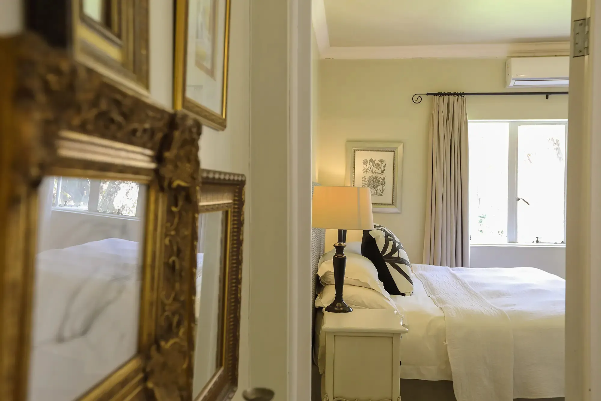 Bedroom with white bed lamp and window with curtains seen through a doorway