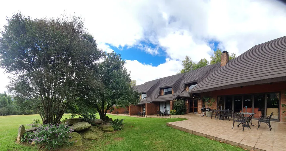 Large house with patio garden and trees under a partly cloudy sky