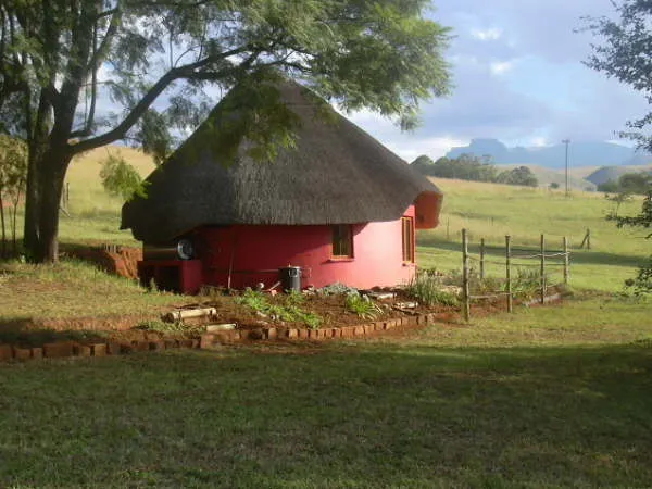 Red round hut with a thatched roof in a green rural landscape