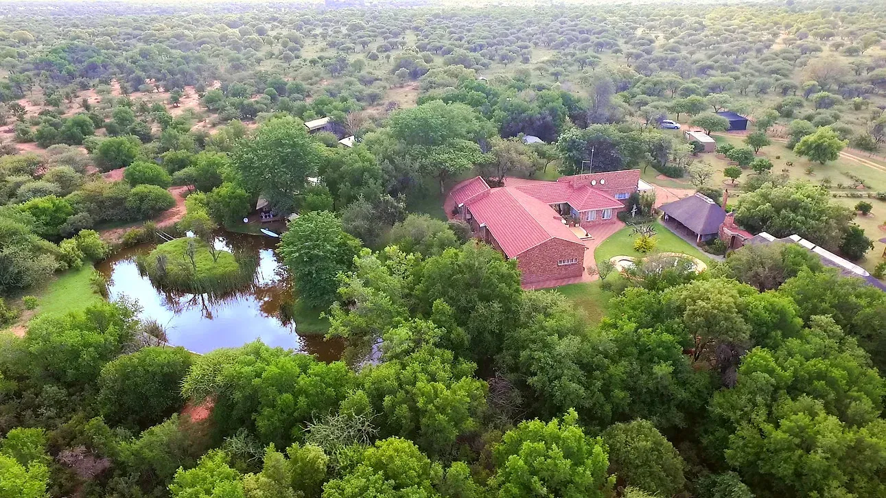 Aerial view of a house surrounded by trees and a pond in a forest