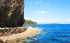 Rocky cliff beside a sandy beach with clear blue ocean and sky
