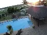 Swimming pool with thatchedroof structure and sunset in the background