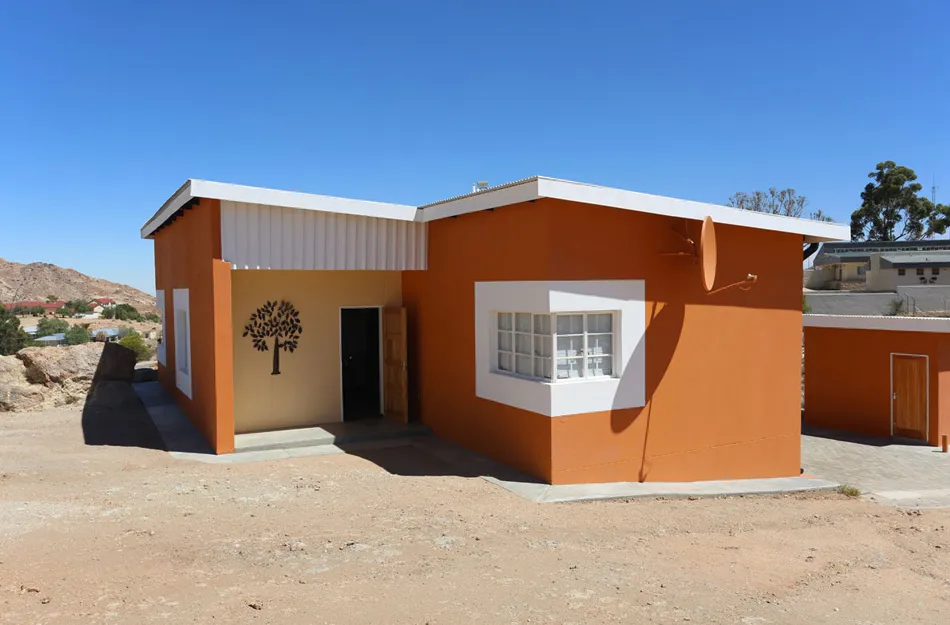 Orange and white building with tree silhouette and desert landscape in background