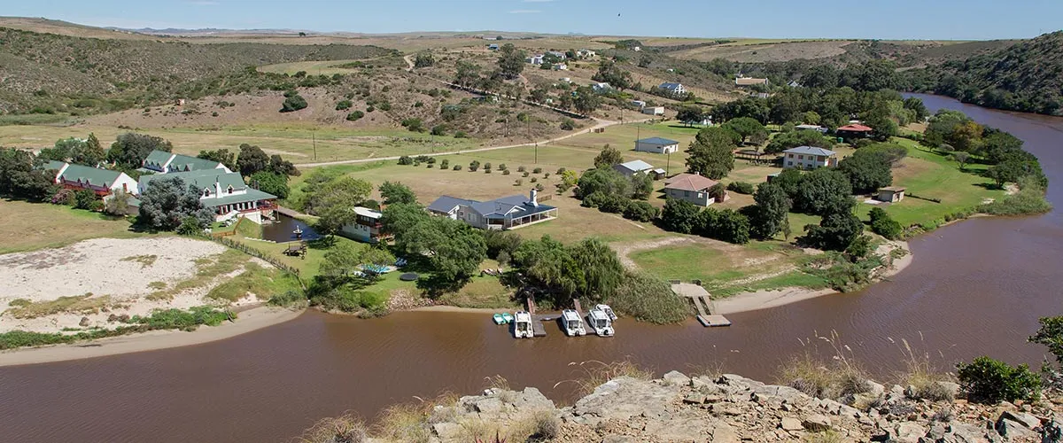 Riverside settlement with houses trees and boats on a calm riverbank