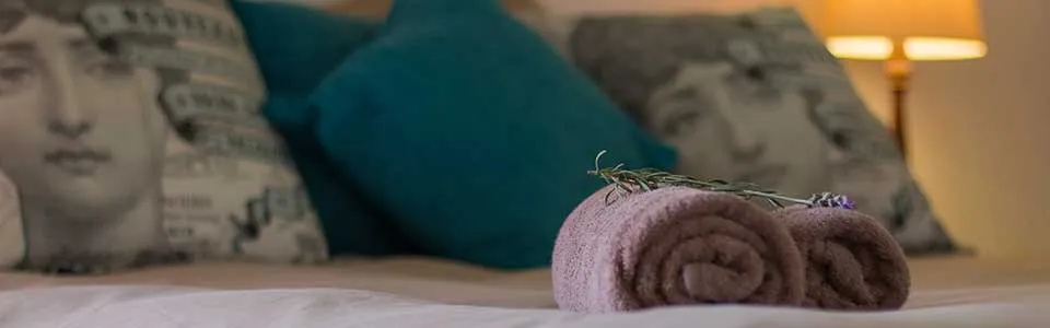 Rolled towels with lavender on a bed with decorative pillows in the background