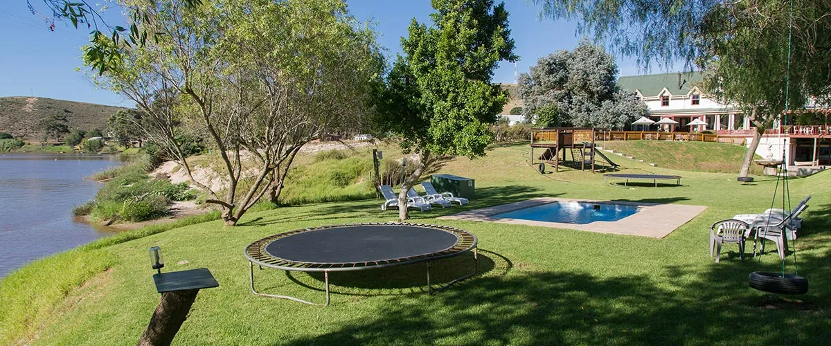 Trampoline in a lush garden with a pool river and house in the background