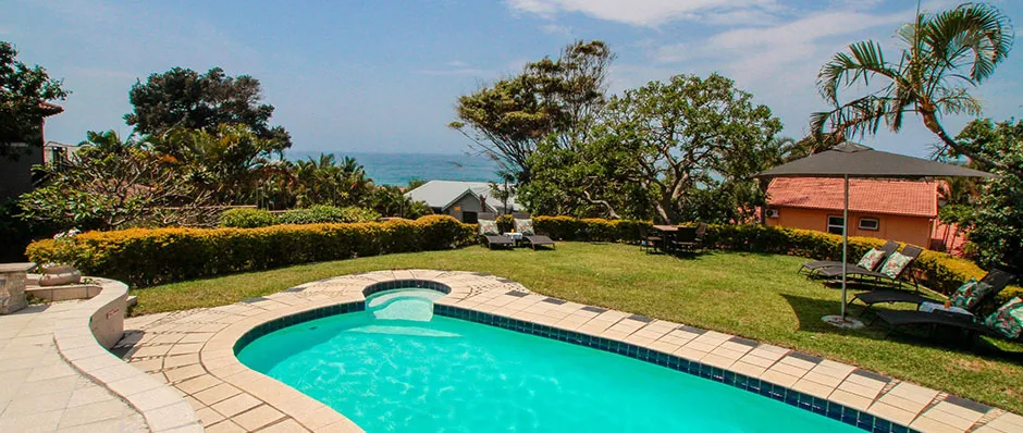 Swimming pool with lounge chairs in a garden overlooking the ocean