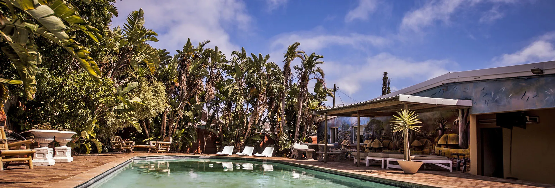Swimming pool surrounded by tropical plants and lounge chairs under a clear sky