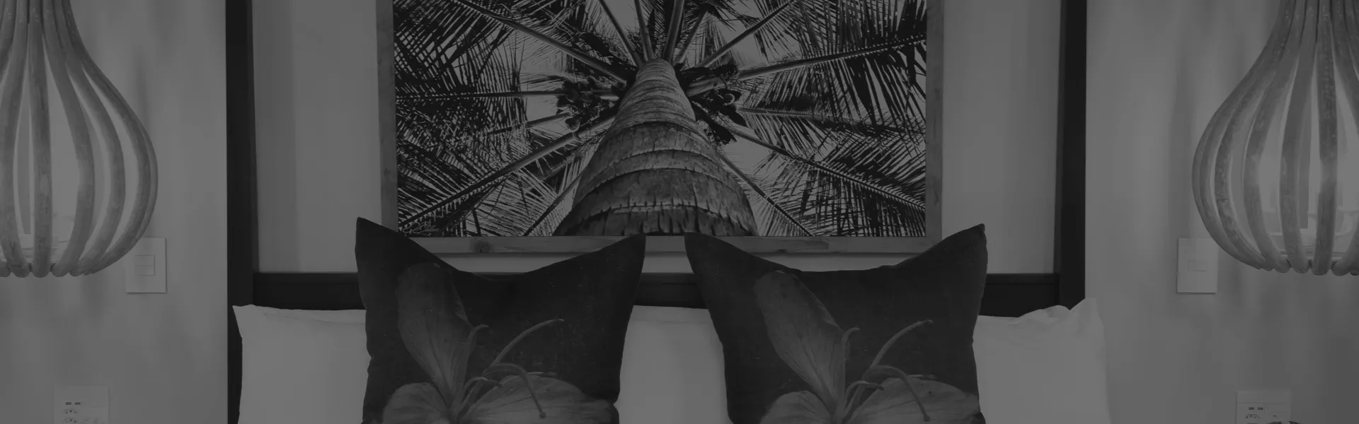 Black and white bedroom with tropical artwork above pillows and hanging lamps