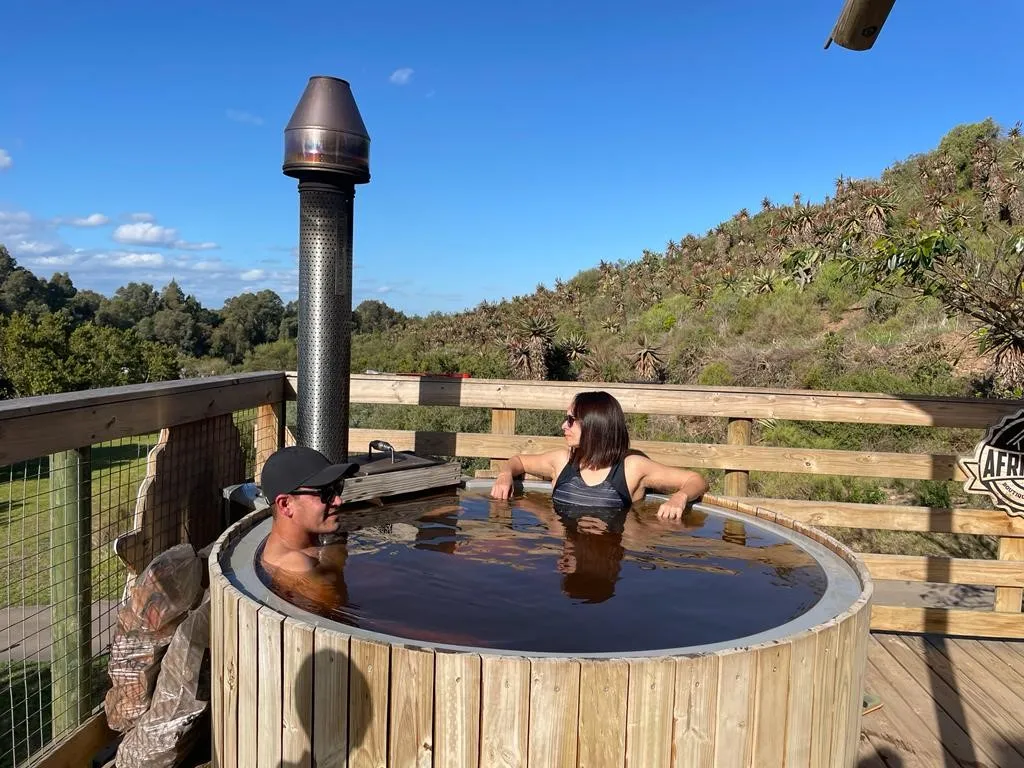 Two people relaxing in a wooden hot tub with a scenic background