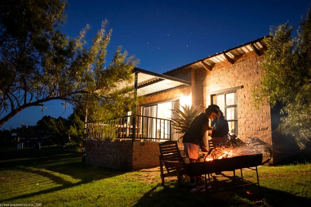 People grilling outside a brick house at night with trees around