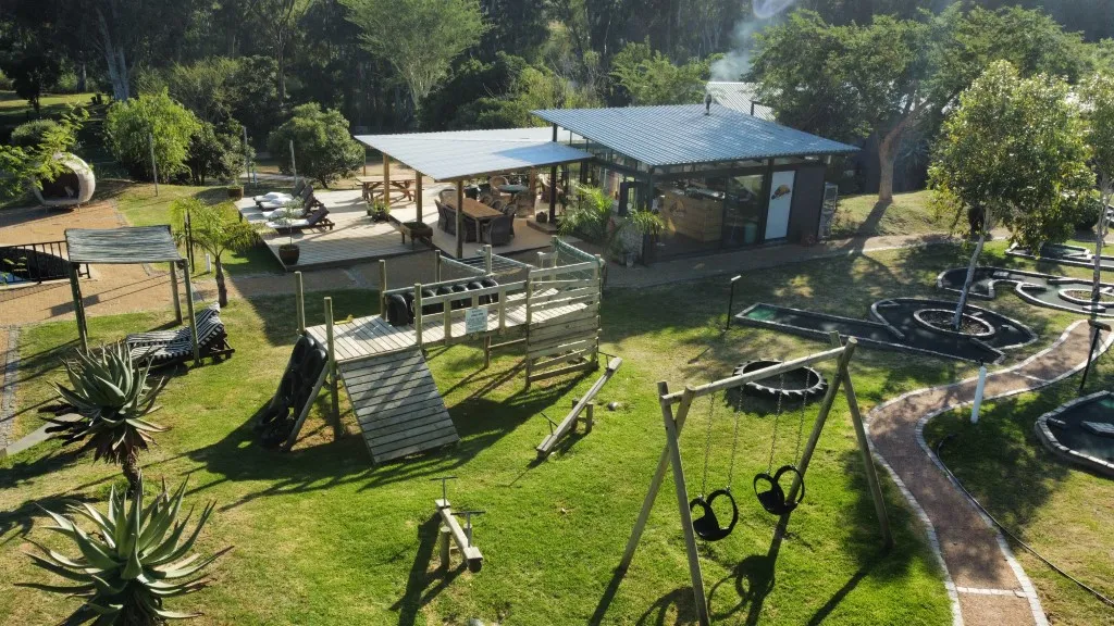 Playground with swings slides and a small building surrounded by greenery