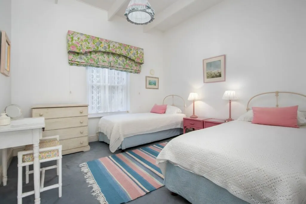 Twin beds in a bright bedroom with floral valance and striped rug