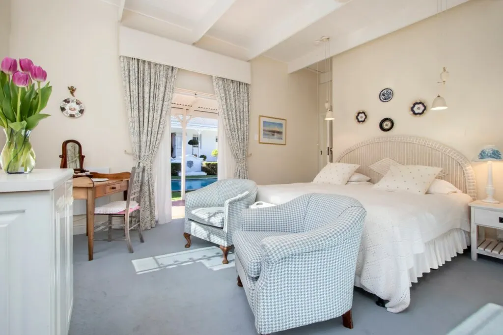 Bedroom with two armchairs bed and French doors leading to a garden