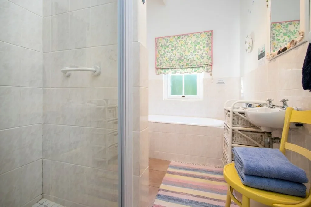 Small bathroom with shower bathtub sink and a yellow chair with blue towels