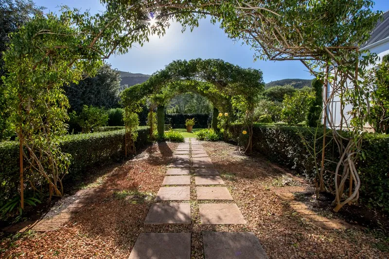 Garden path with archways covered in greenery and flowers sunny day