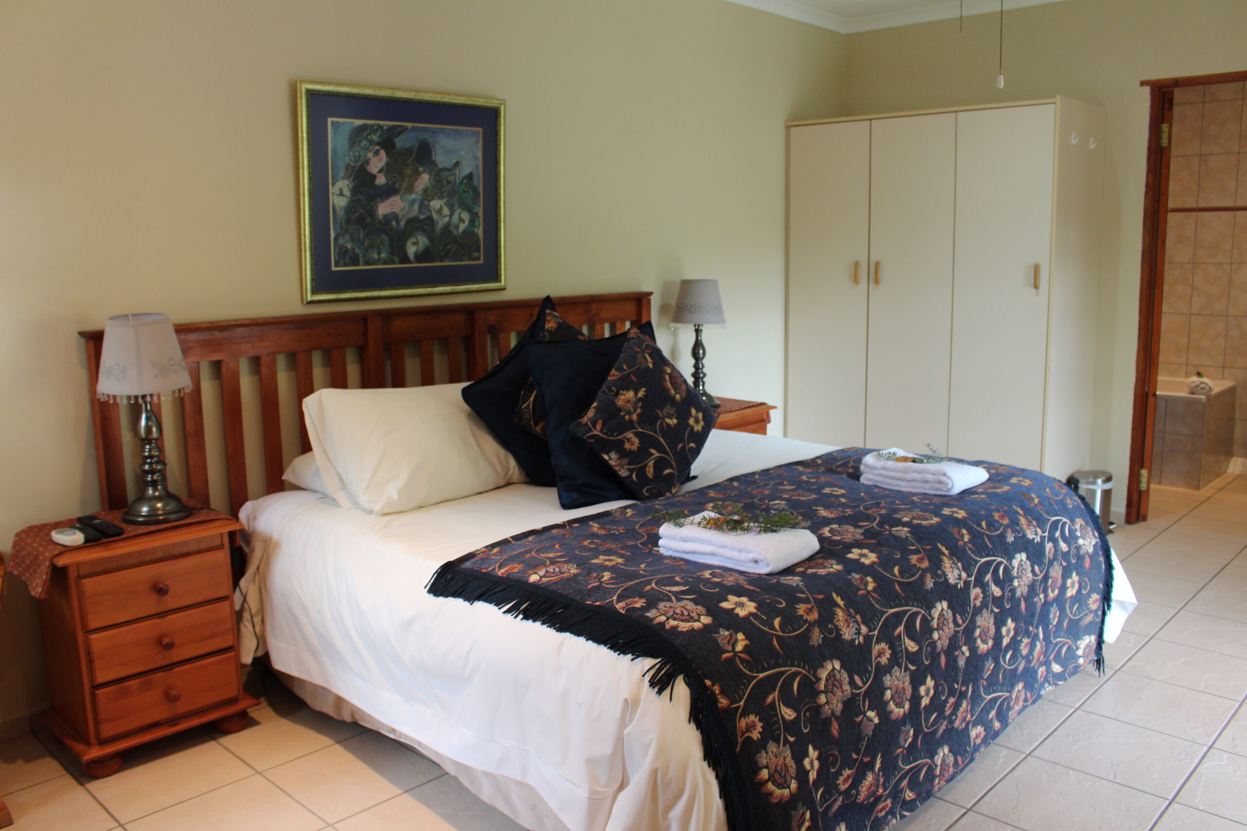 A neatly made bed in a tidy bedroom with floral decor and wooden furniture.
