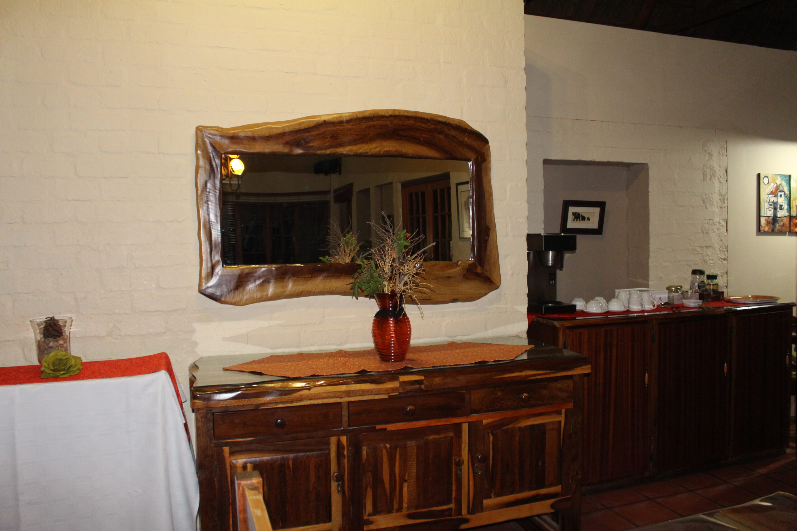 Wooden furniture with mirror, flowers, and coffee maker in a cozy room.