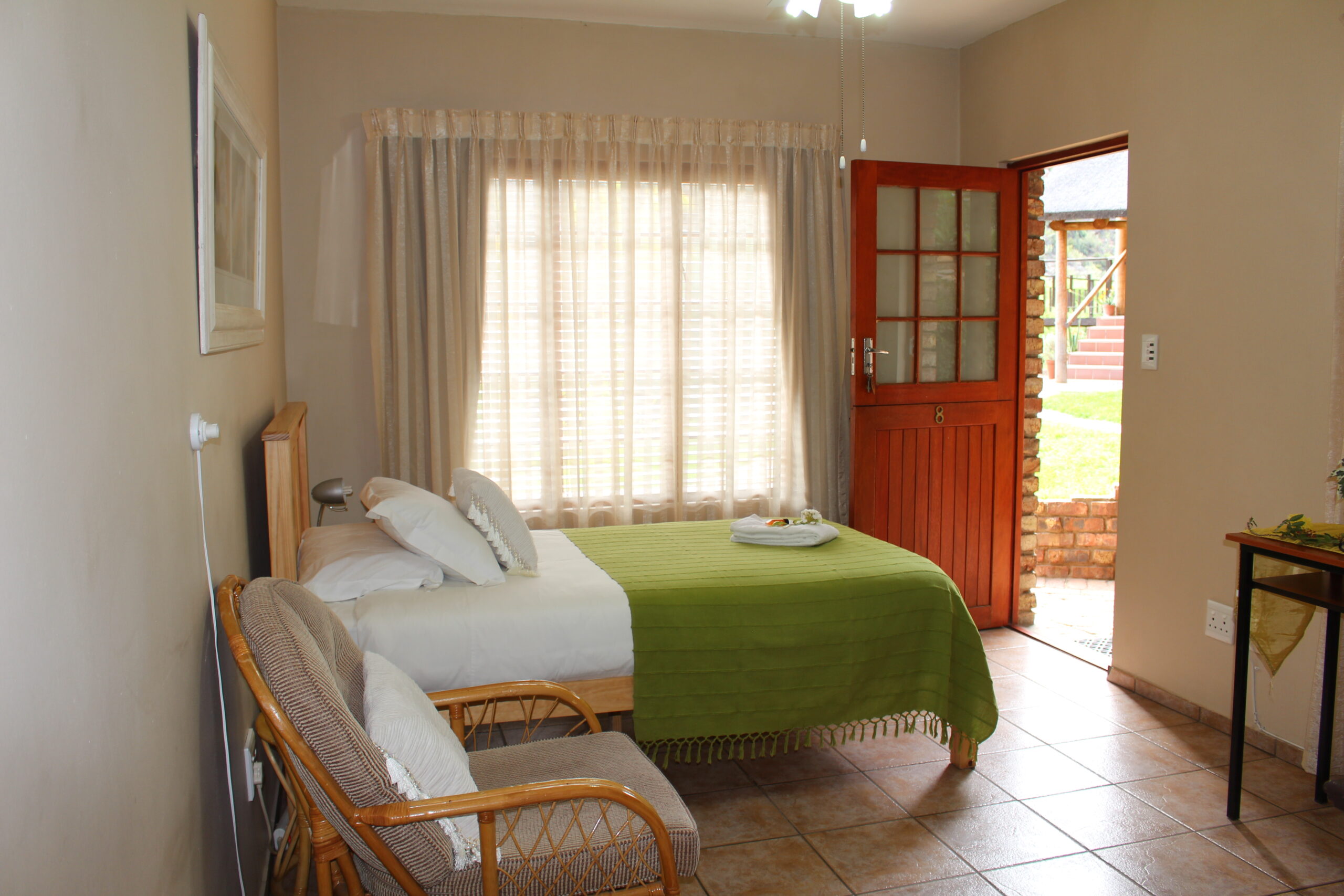 Cozy bedroom with a single bed, armchair, and open wooden door to outside.