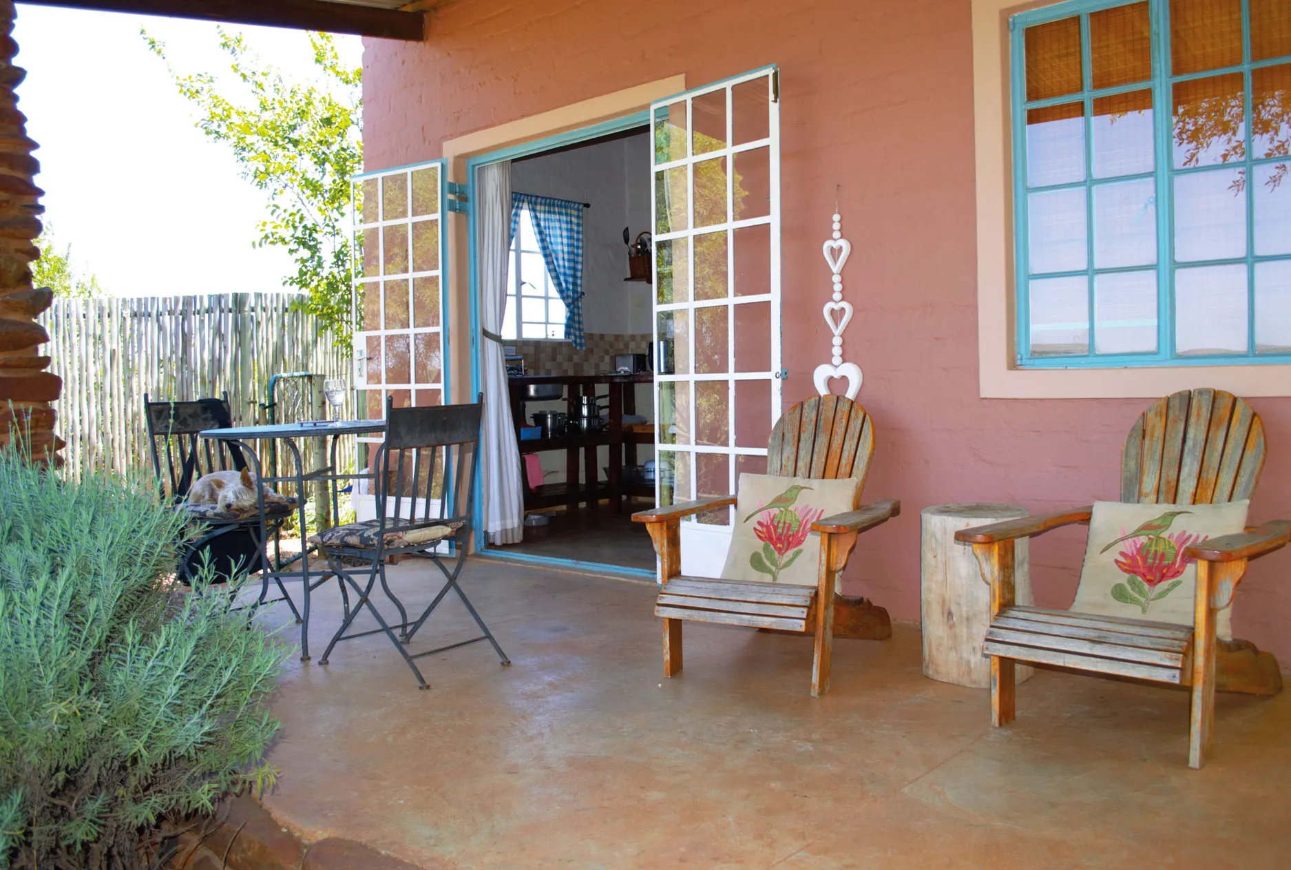 Two wooden chairs with floral cushions on a patio outside a pink house