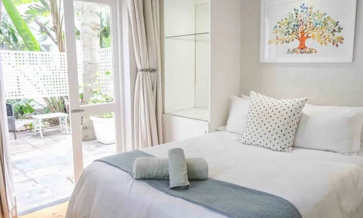 Bright bedroom with white bed colorful tree artwork and open patio doors