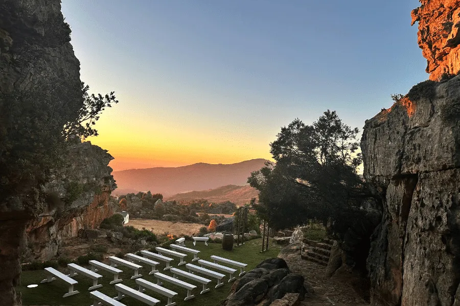 Outdoor wedding setup with white chairs between rocky cliffs at sunset