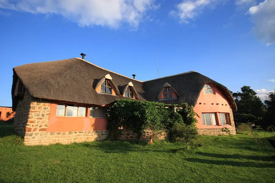 Thatchedroof house with stone and red walls in a grassy area under blue sky