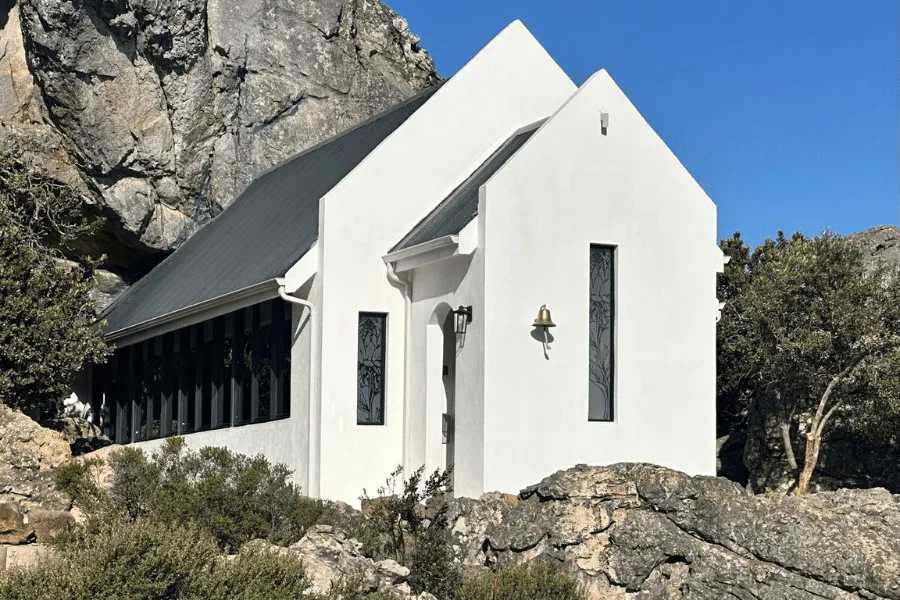 White church with tall windows built against a rocky mountain backdrop