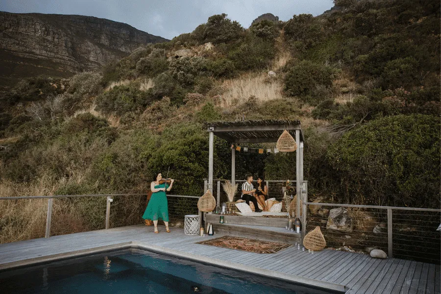 Woman photographing couple in a hillside setting with a pool and greenery