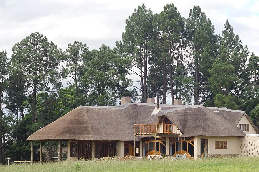Thatchedroof house with wooden balcony surrounded by tall trees and greenery