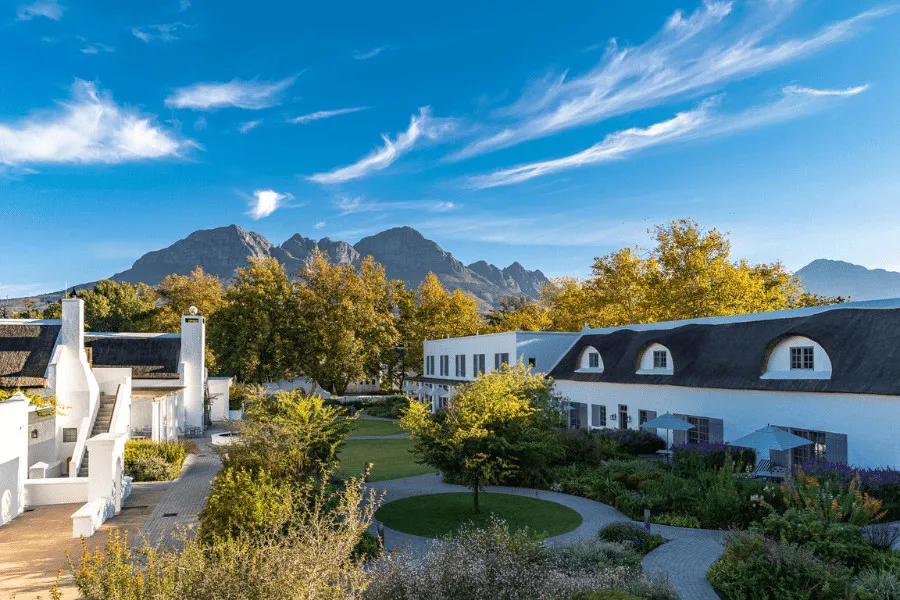White buildings with dark roofs green lawns and mountains under a blue sky