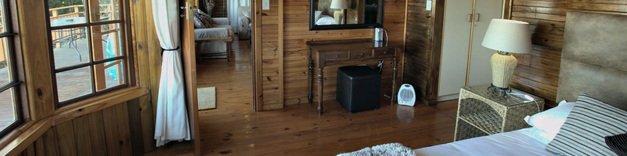 Wooden bedroom with large windows bed lamp and adjacent living area