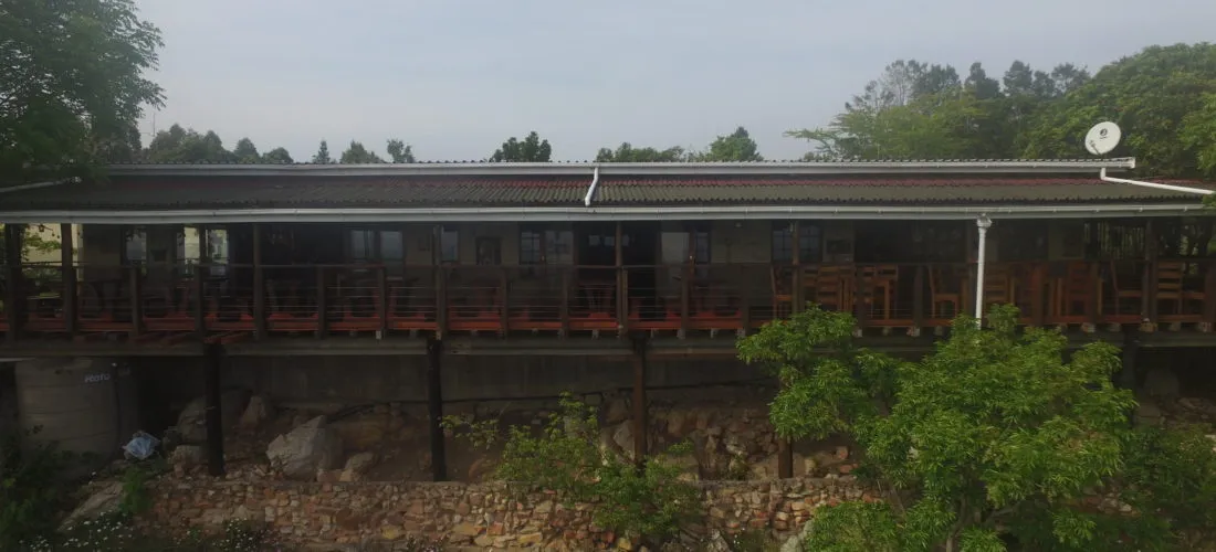 Long wooden building with a veranda surrounded by greenery and rocks
