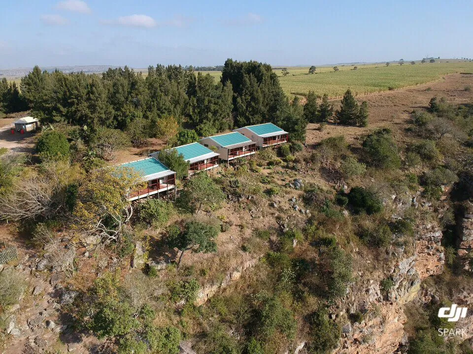 Three greenroofed cabins on a cliff overlooking fields and trees