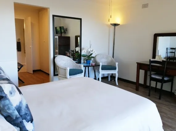 Bright bedroom with white bed seating area mirror and wooden desk