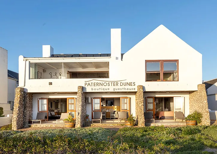 White twostory guesthouse with stone pillars and wooden balconies blue sky background