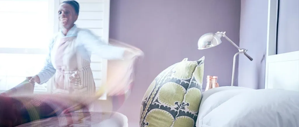 Woman dancing in a bedroom with a bed and lamp in the background