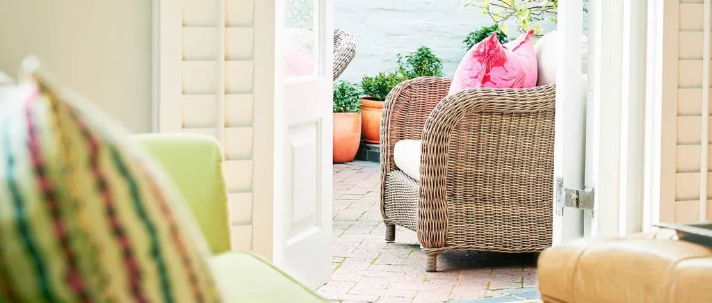 Wicker chair with pink cushion on patio green chair in foreground