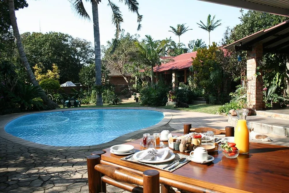 Outdoor breakfast table with pool tropical plants and buildings in the background