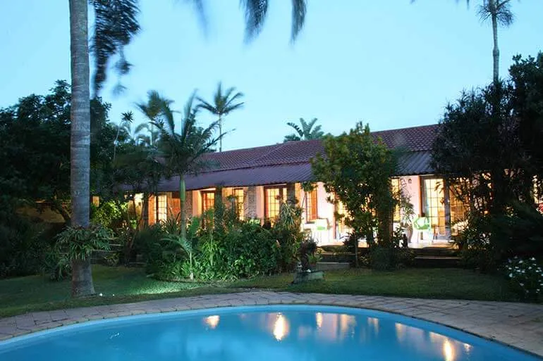 House with lit windows and palm trees at dusk with a pool in foreground