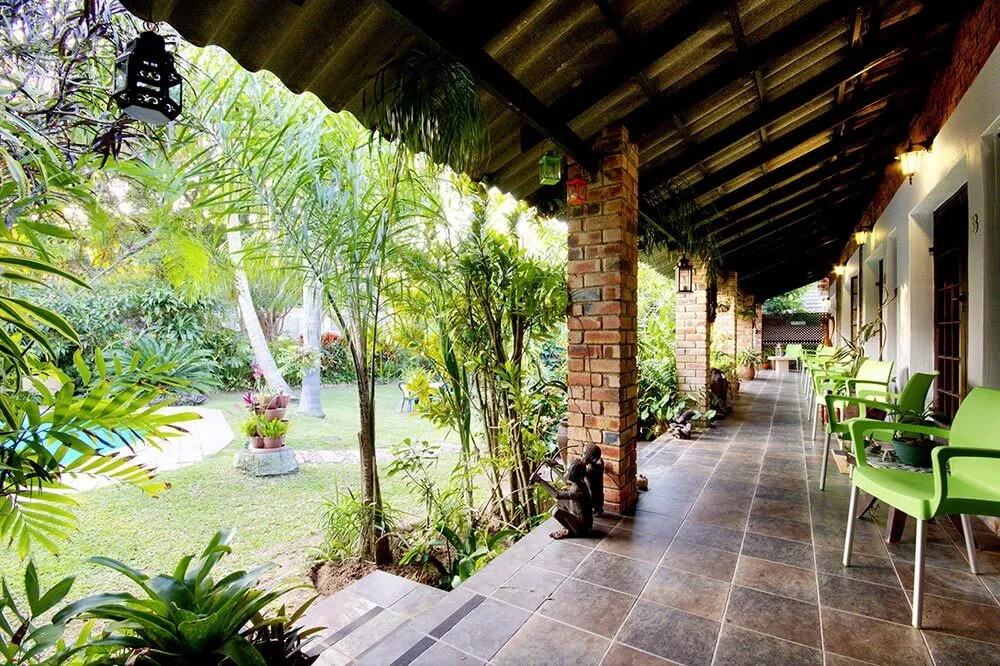 Covered patio with green chairs overlooking a lush garden with a pool