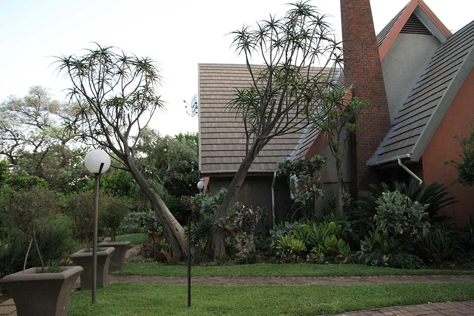 House with a red brick chimney and lush garden with palm trees