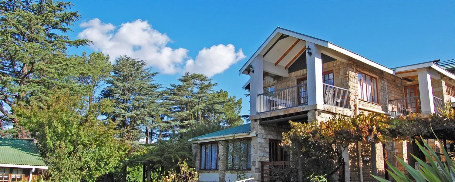 Twostory stone house with a balcony surrounded by trees under a blue sky