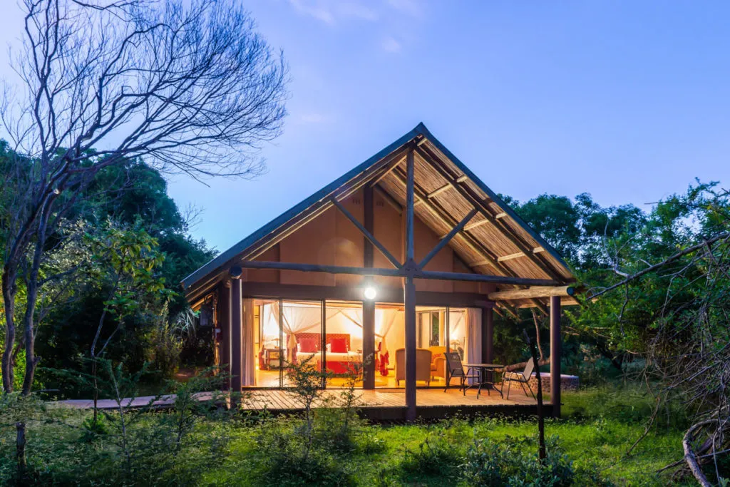 Wooden cabin with large windows lit up at night surrounded by trees